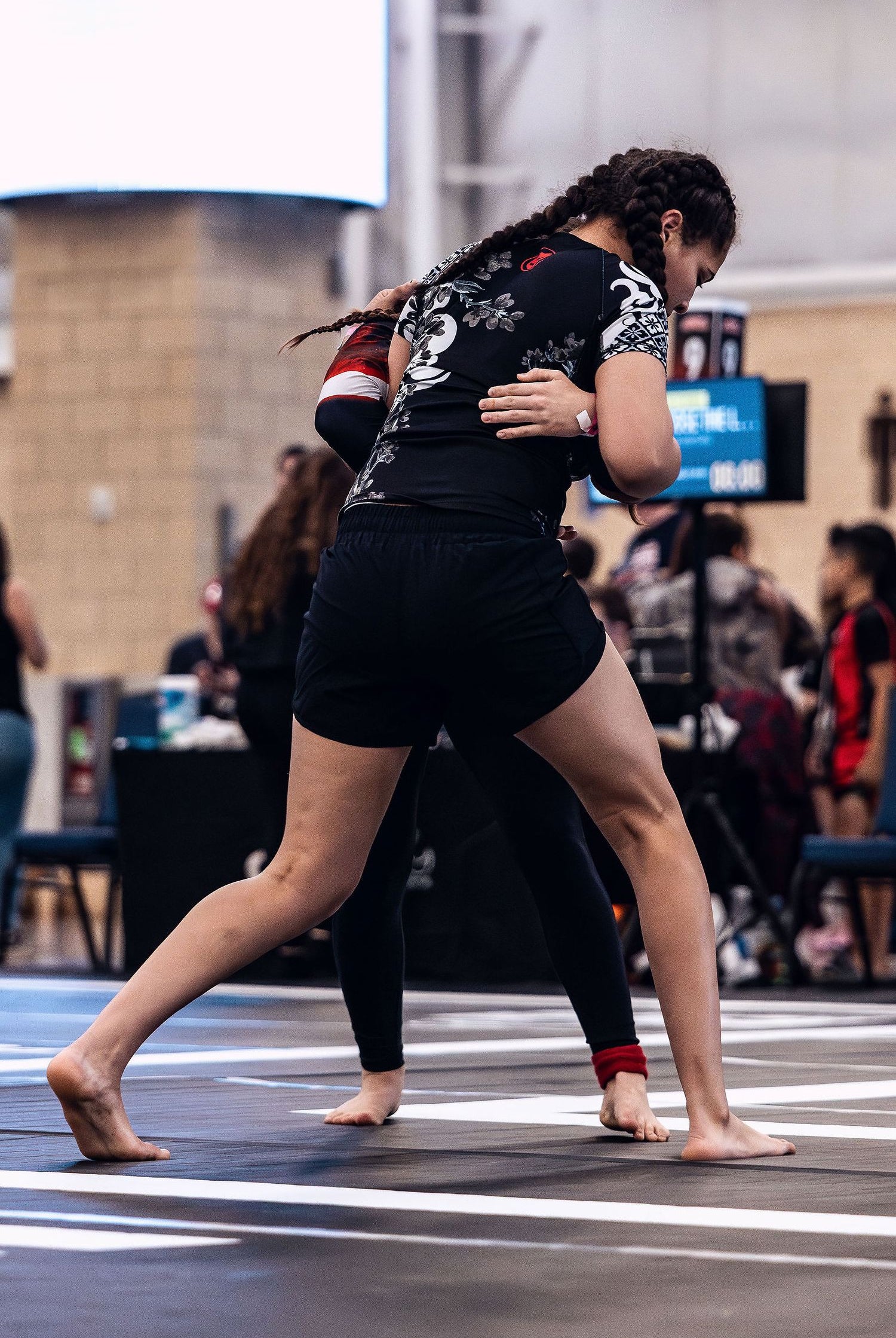 Young woman wearing a floral BJJ black belt ranked rashguard and black Jiu Jitsu shorts for women while wrestling at an ADCC Open competition.