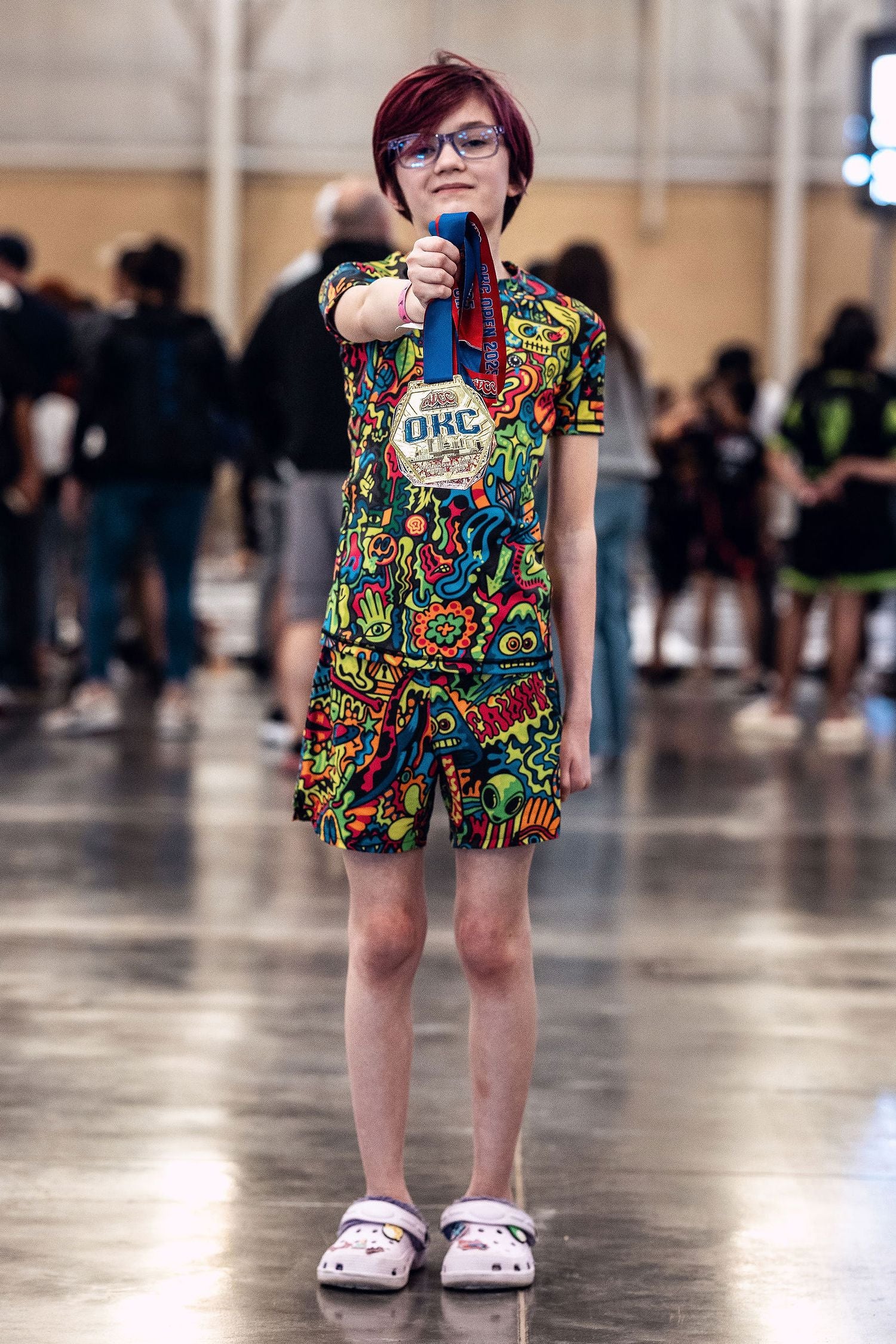 Young girl wearing Gaidama's Psychedelic Wotto Doodle kids rashguard and youth BJJ shorts holding up her competition medal at an ADCC Open nogi Jiu Jitsu tournament.