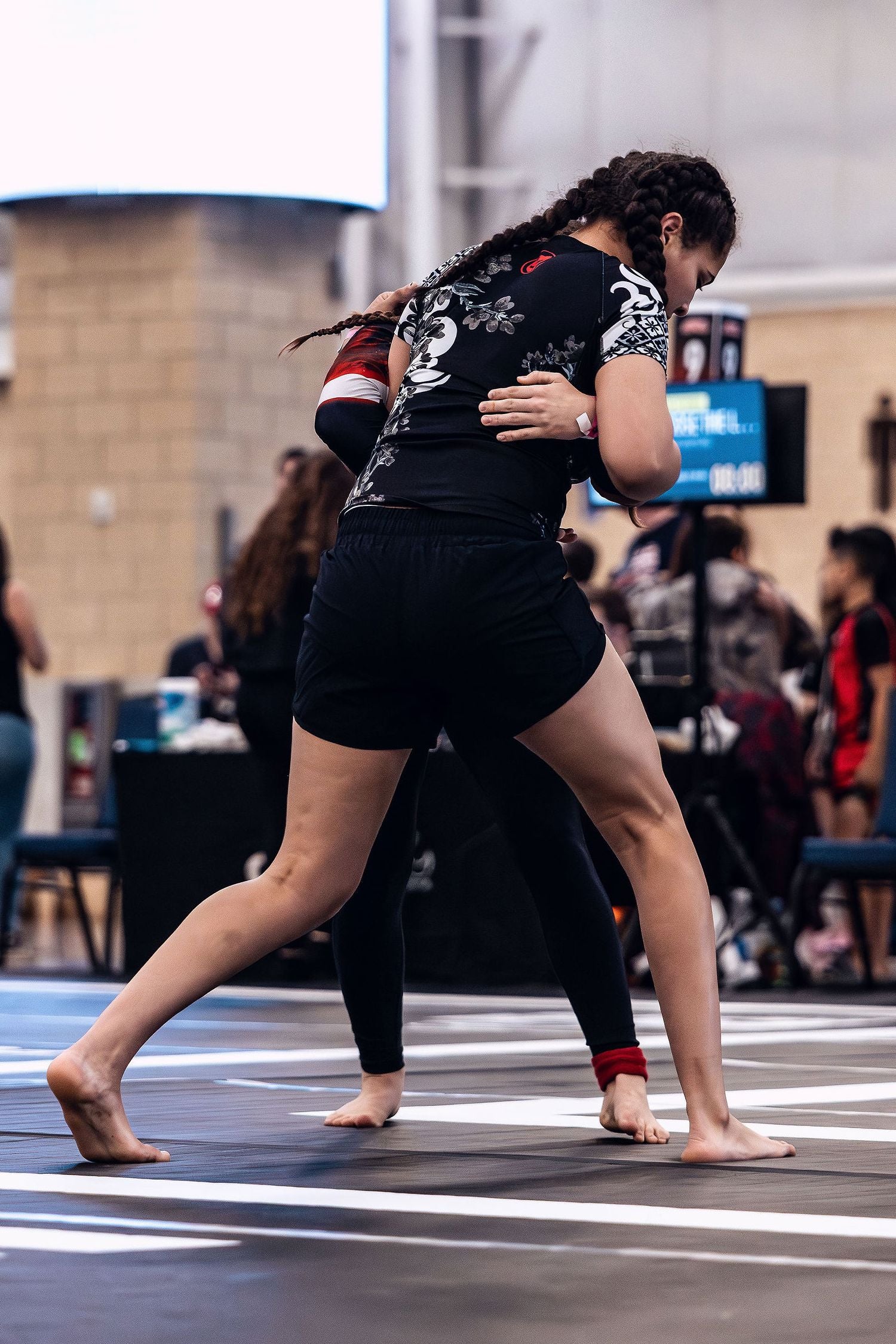 Young woman wearing a floral BJJ black belt ranked rashguard and black Jiu Jitsu shorts for women while wrestling at an ADCC Open competition.