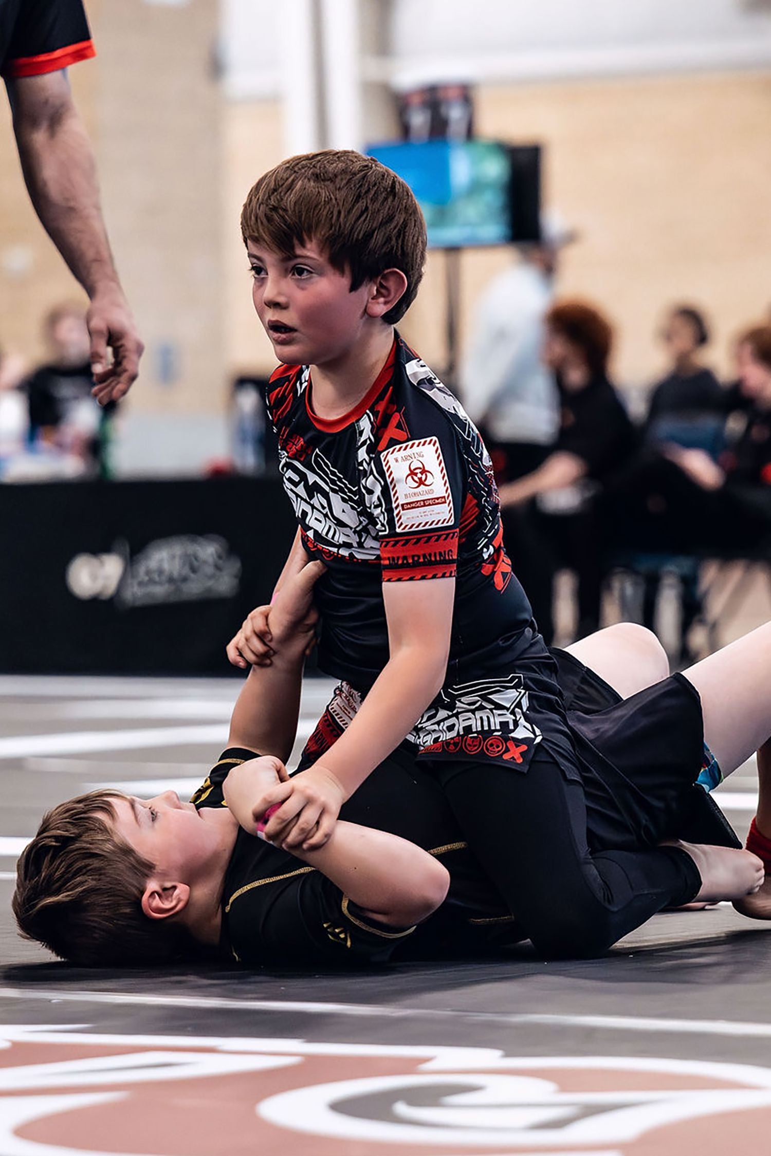 Young boy wearing Gaidama's black, red, and white nogi BJJ set for children, pinning another youth competitor in the mount position at an ADCC Open Jiu Jitsu tournament.
